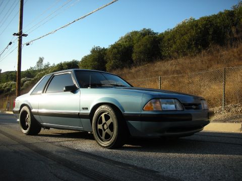 1990 Ford Mustang - 1990 Ford Mustang coupe with aftermarket wheels parked on a road with tire marks.