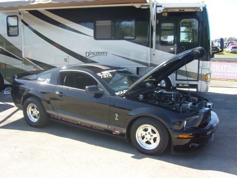 2007 Ford Mustang - A black Ford Mustang GT 500 is parked with its hood open, beside a large RV.
