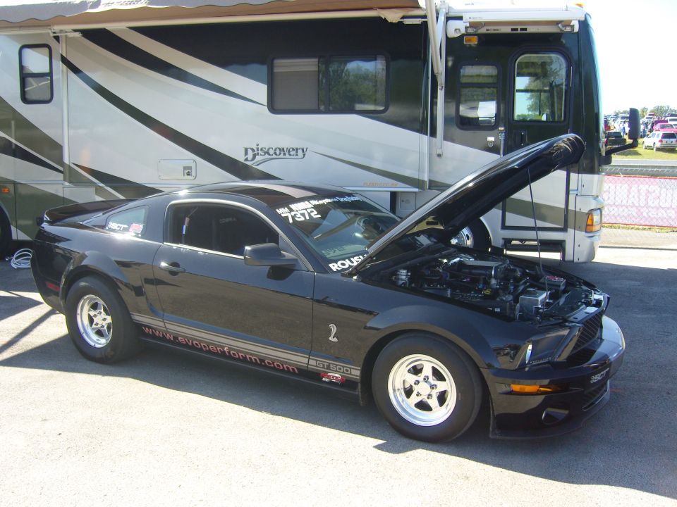 Black Ford Mustang GT 500 with hood open, parked next to an RV