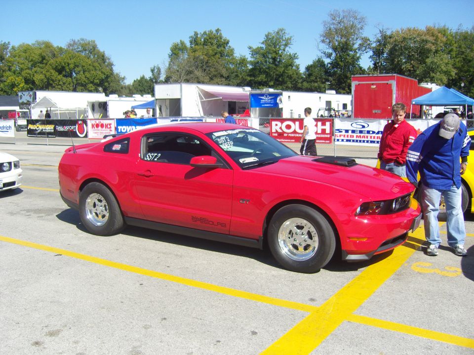 Red 2007 Ford Mustang with racing slicks and hood scoop parked at a drag strip