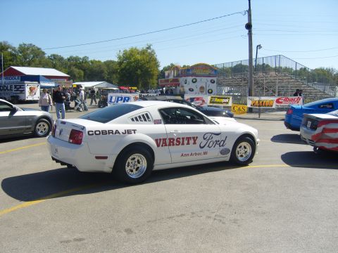 2007 Ford Mustang - A white Ford Mustang with racing decals is parked at a track event.