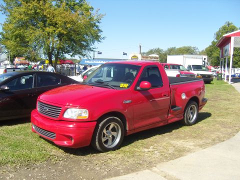 2007 Ford Mustang - Red 2000 Ford F-150 SVT Lightning pickup truck with aftermarket wheels is parked outside.