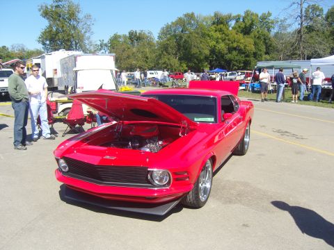 2007 Ford Mustang - A bright red classic car is displayed with its hood open, revealing the engine bay. The car is parked outdoors at an event.