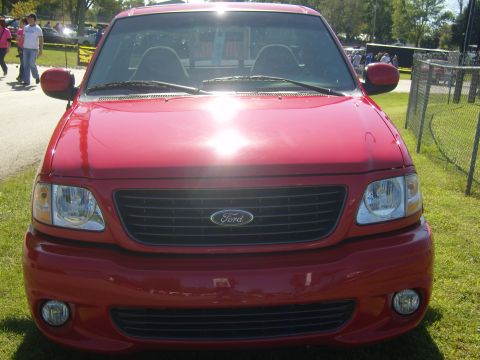 2007 Ford Mustang - A red Ford F-150 SVT Lightning pickup truck is parked on grass with a fence in the background.