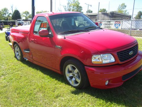 2007 Ford Mustang - A red pickup truck is parked on a grassy area with a "For Sale" sign visible in the driver's side window.