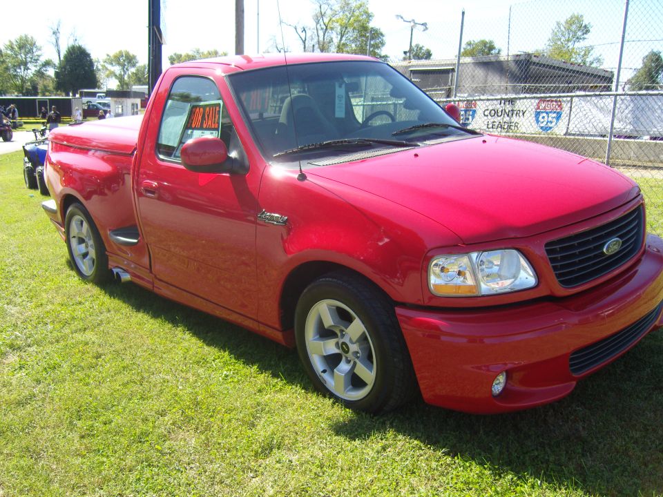 Red pickup truck with a "For Sale" sign in the window, parked on grass