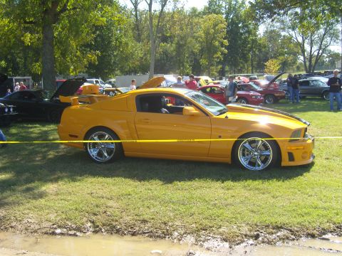 2007 Ford Mustang - A yellow 2007 Ford Mustang is displayed at an outdoor car show with other vehicles in the background.