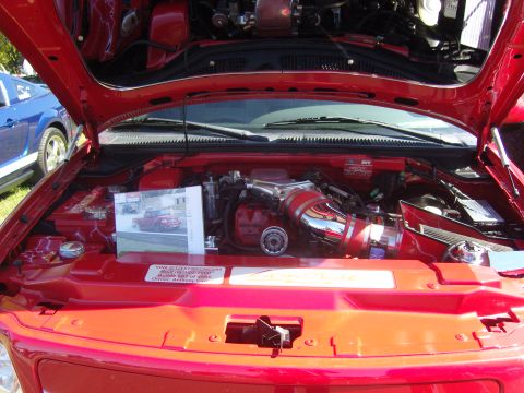 2007 Ford Mustang - The engine bay of a red truck is open, revealing its engine and a display photo, with a blue Mustang visible to the side.