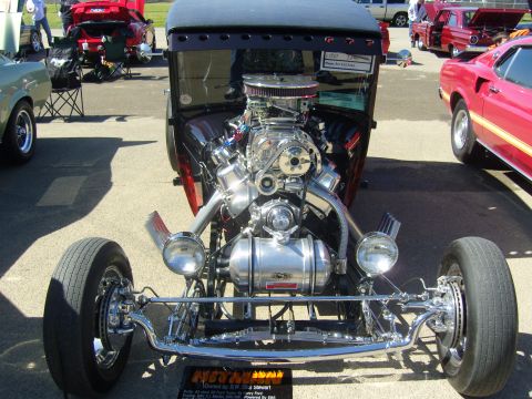 2007 Ford Mustang - A custom hot rod with a prominent supercharged engine is displayed at a car show, with other vehicles visible in the background.