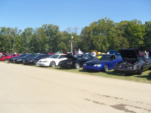 2007 Ford Mustang - A lineup of Ford Mustangs, including a gray convertible with its hood open, is displayed under a clear blue sky.