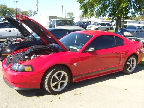 2007 Ford Mustang - A red Ford Mustang is parked with its hood open, alongside another car also showing its engine. The scene appears to be an outdoor car show.