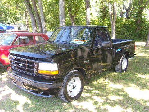 2007 Ford Mustang - A black Ford F-150 pickup truck is parked outside with a red car nearby.