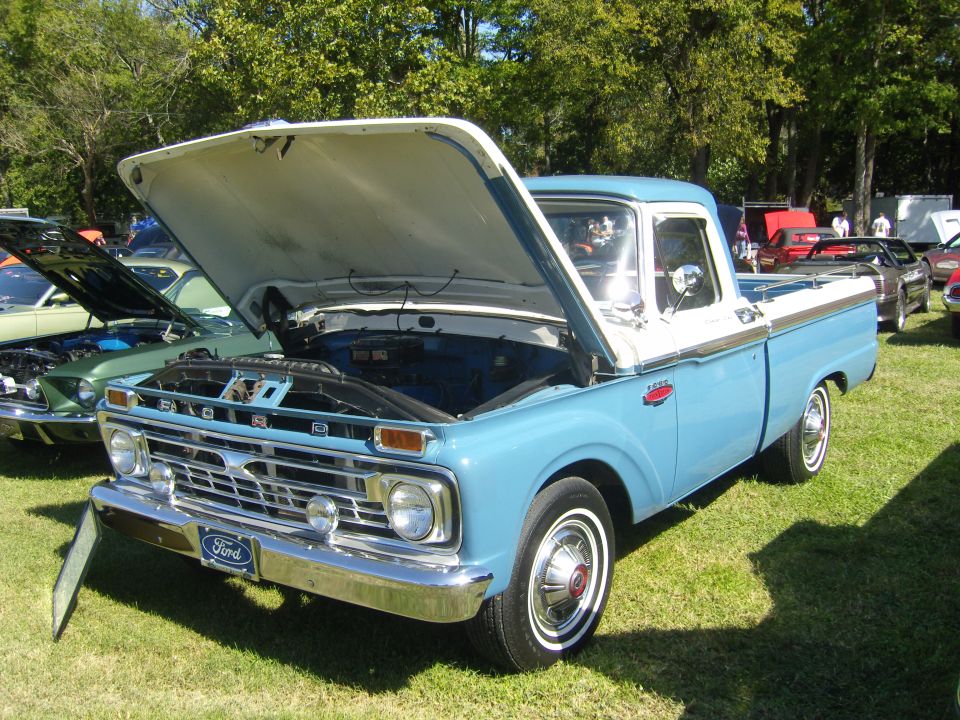 Blue and white Ford F-series pickup truck, hood open, parked on grass at a car show