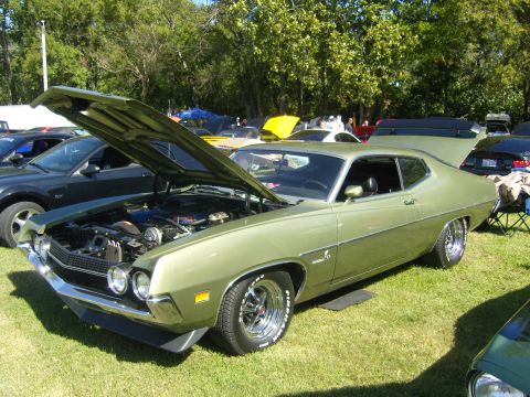 2007 Ford Mustang - A classic green Ford Torino GT is displayed with its hood open at a car show, surrounded by other vehicles.