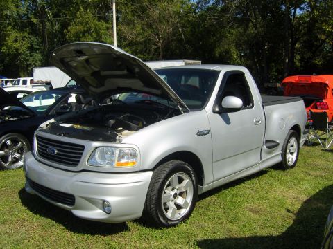 2007 Ford Mustang - Silver Ford F-150 SVT Lightning regular-cab stepside pickup parked on grass at an outdoor car show with its hood raised. It wears the facto…