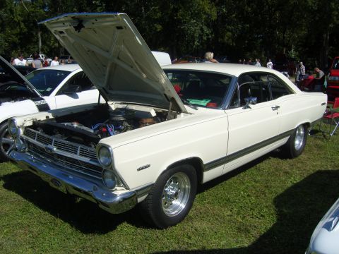 2007 Ford Mustang - A white 1967 Ford Fairlane 500 is displayed with its hood open, revealing the engine bay. Another car is visible to the left.
