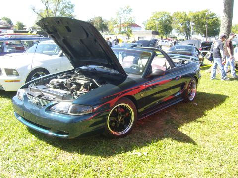 2007 Ford Mustang - A dark green convertible Mustang with racing stripes is parked on grass with its hood open, revealing the engine bay.