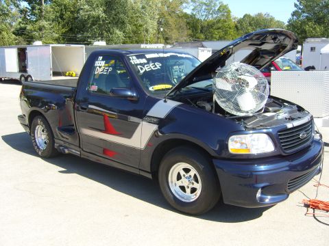 2007 Ford Mustang - A dark blue Ford F-150 Lightning pickup truck is parked with its hood open, revealing a large fan positioned in the engine bay.