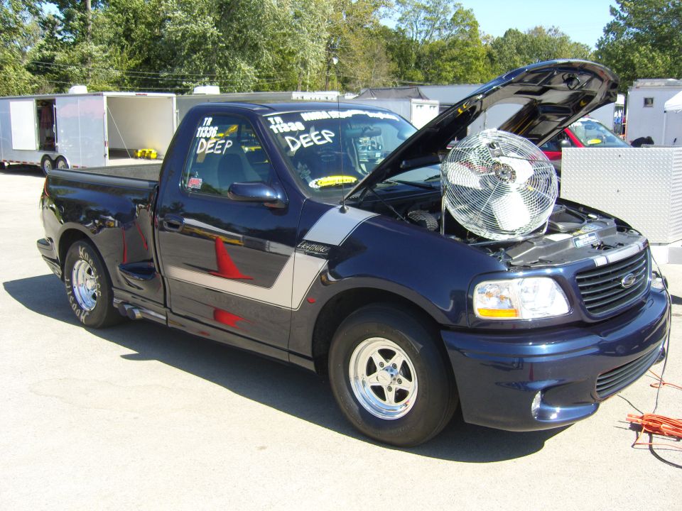 Dark blue Ford F-150 Lightning pickup truck with hood open and a fan inside, parked outside