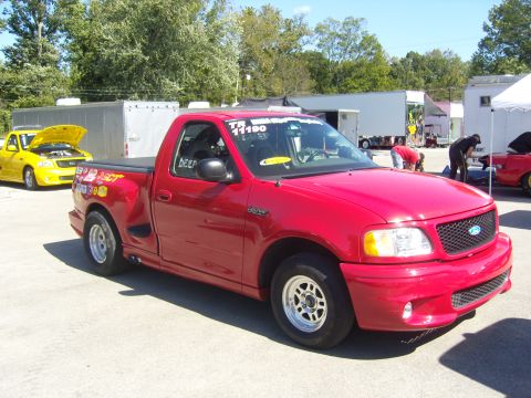2007 Ford Mustang - A red pickup truck is parked at an outdoor event, with other vehicles and people in the background.