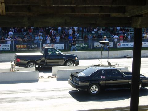2007 Ford Mustang - Two vehicles compete in a drag race event, with a crowd watching from the stands.