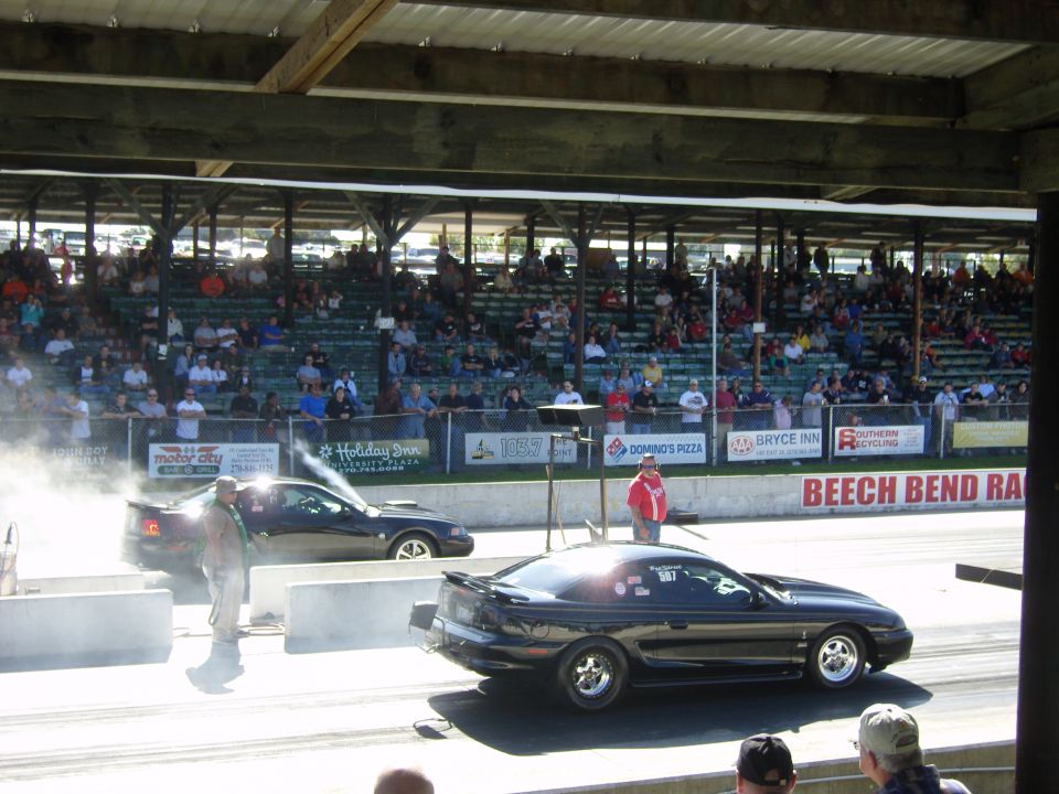 Black Mustang drag racing, smoke coming off tires. Another Mustang is to the left