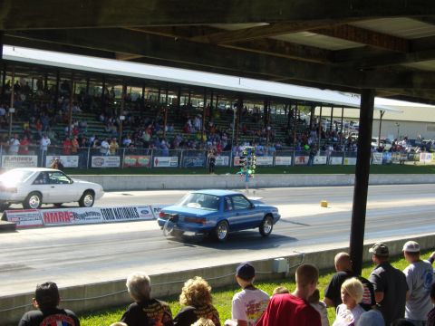 2007 Ford Mustang - Two cars race down a drag strip in front of a grandstand filled with spectators.