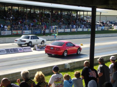 2007 Ford Mustang - Two cars compete in a drag race at a track with grandstands full of spectators.
