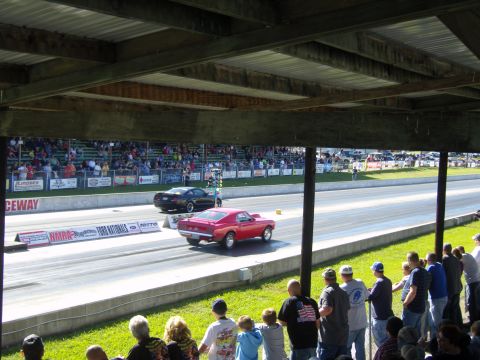 2007 Ford Mustang - Two cars compete on a drag strip with spectators in the background.