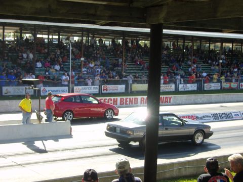2007 Ford Mustang - Two cars race down a drag strip with a crowd watching from the stands.