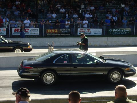 2007 Ford Mustang - A black coupe with racing numbers on its door is seen on a drag strip, with another vehicle visible in the background.