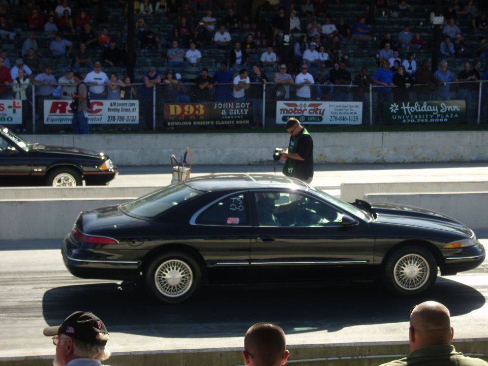 Black coupe with racing numbers on door, side view on drag strip