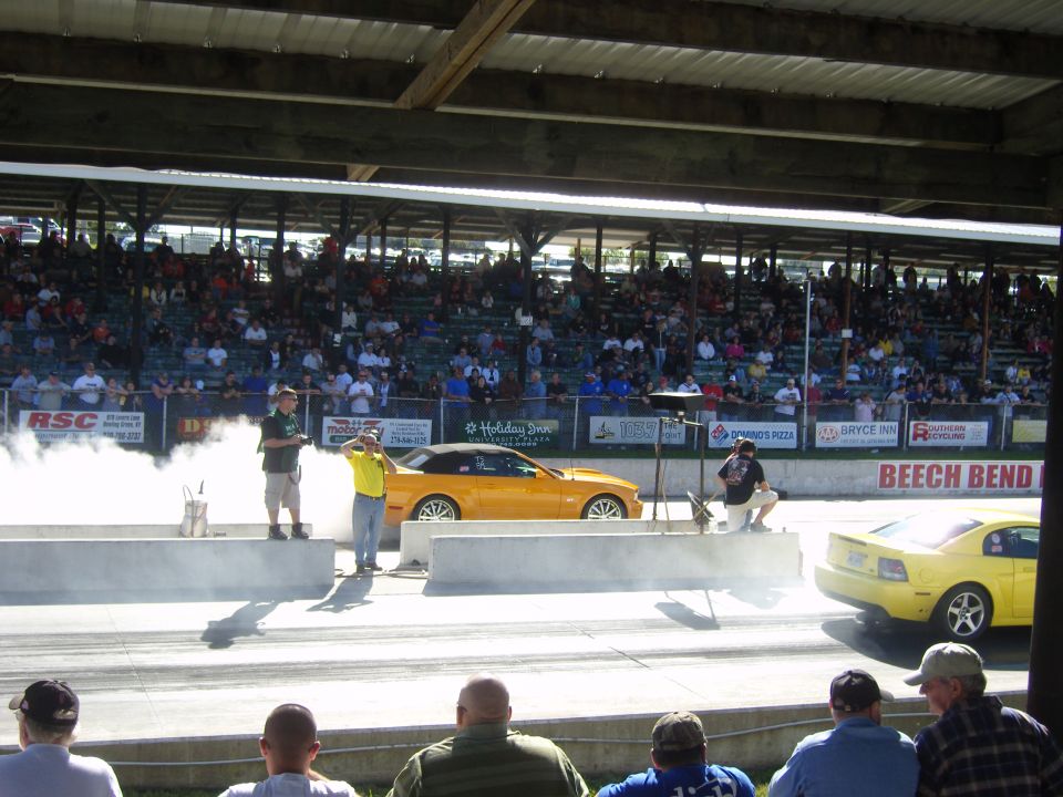 yellow convertible and coupe drag racing, crowd in bleachers