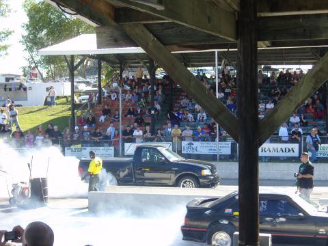 2007 Ford Mustang - Two vehicles prepare for a drag race, with spectators watching from the stands.