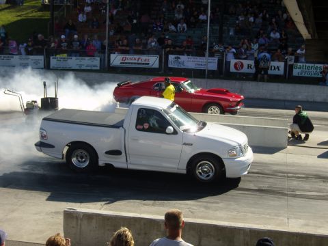 2007 Ford Mustang - Two vehicles prepare for a drag race, surrounded by spectators and smoke.