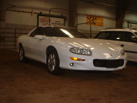2000 Ford Crown Victoria - A white Chevrolet Camaro is parked inside a building, with another vehicle visible behind it.
