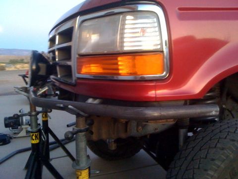 1989 Ford Bronco - Front end of a red 1989 Ford Bronco, modified with a custom bumper and supported by jack stands.