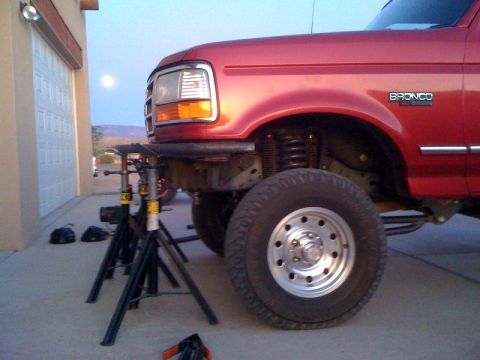 1989 Ford Bronco - This red Ford Bronco is elevated on jack stands for maintenance, with a full moon visible in the twilight sky.
