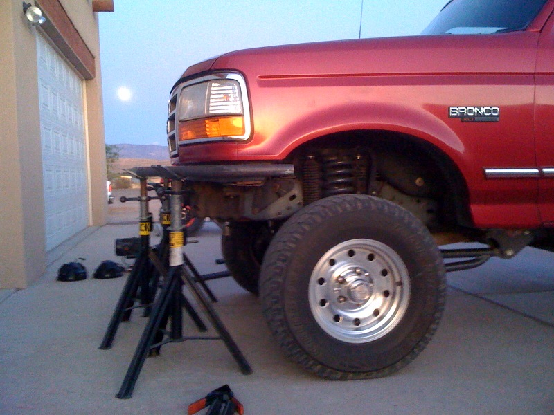 Red Ford Bronco on jack stands in front of a garage. Moon visible in the sky