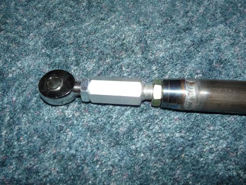 1994 Ford F-150 - Close-up of one end of a fabricated suspension link lying on green carpet, showing a heim joint rod end threaded into a hex adapter bushing…
