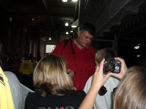 1979 Ford F-150 - A man in a red shirt is signing autographs for fans at an event. A person in the foreground is taking a photo with a digital camera.