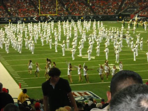 1979 Ford F-150 - A marching band and cheerleaders are performing on a football field during a game.