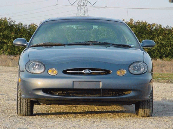 Front view of silver-blue Ford Taurus sedan parked on gravel near power lines