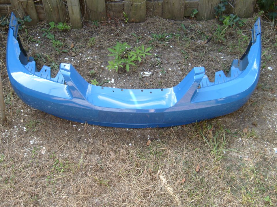 Blue car bumper with mounting brackets visible, lying on the ground