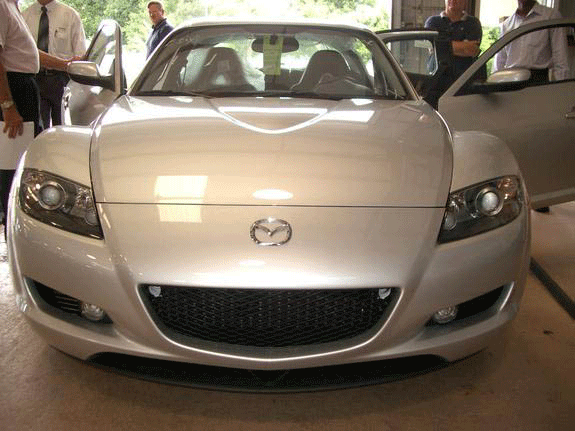 Front of silver Mazda RX-8 sports coupe in a garage with people standing nearby