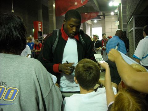 1979 Ford F-150 - A football player signs autographs for fans in a concourse area with team banners overhead.