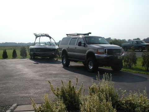 2000 Ford Excursion - A Ford Excursion is parked on a driveway, hitched to a boat on a trailer, with a pickup truck in the background.