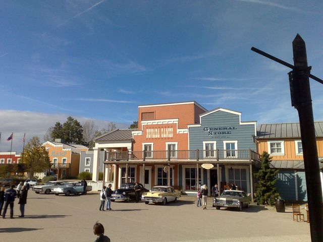 Old west town square with vintage cars parked in front of buildings labeled General Store and Saloon