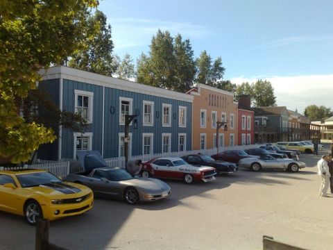 1991 Ford LTD Crown Victoria - Several cars are parked in a row in front of a line of colorful, old-fashioned buildings under a clear blue sky.