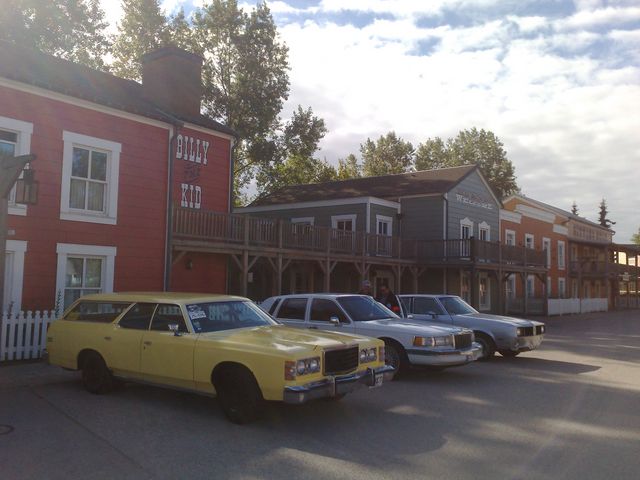 Yellow 1977 Ford Country Squire station wagon parked in front of western-themed buildings